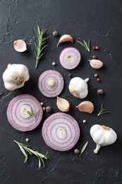 Fresh raw garlic, onion rings and spices on black table, flat lay