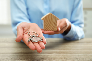 Photo of Real estate agent holding house figure and key at wooden table, closeup