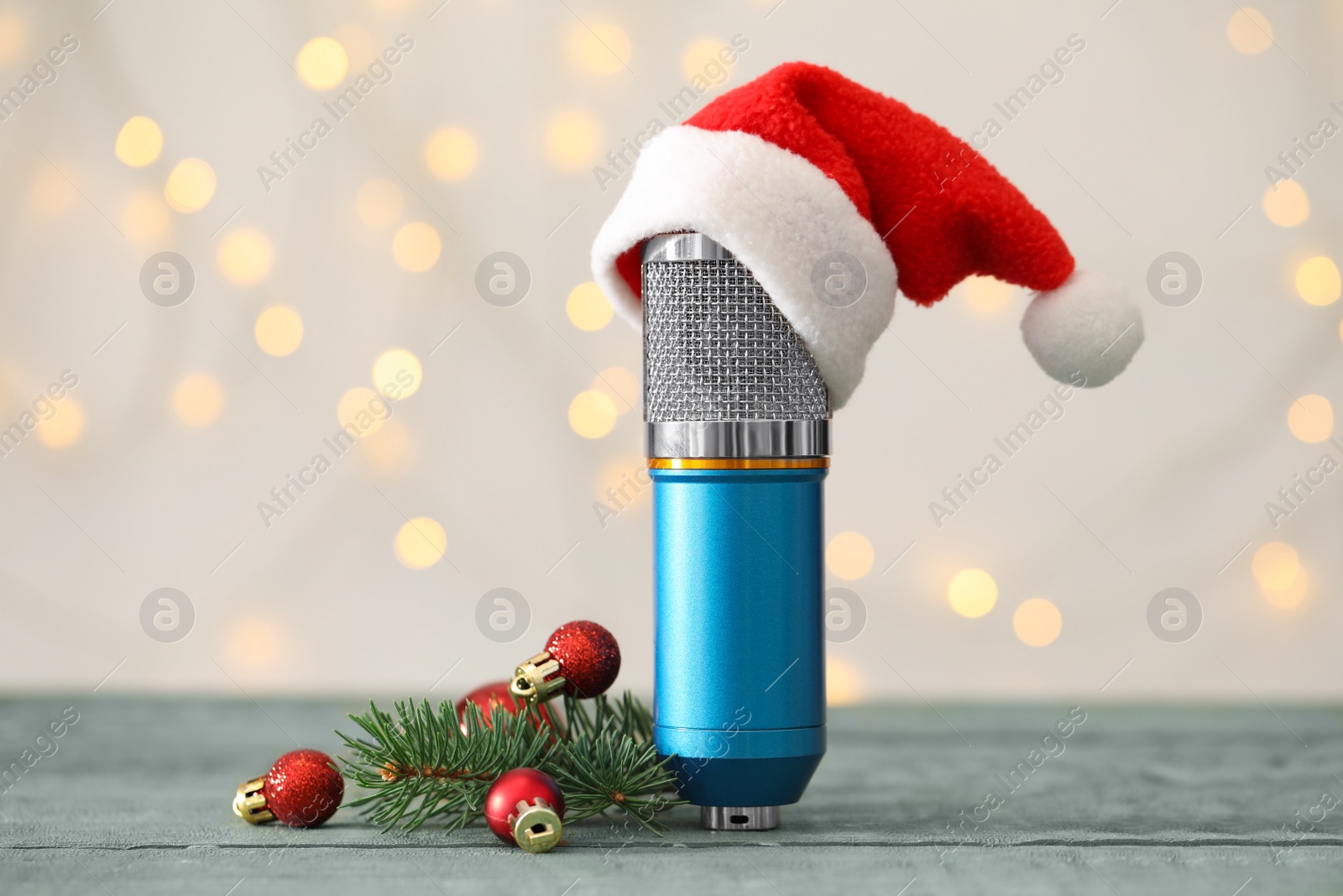 Photo of Microphone with Santa hat and festive decor on blue wooden table against blurred lights. Christmas music