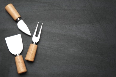 Cheese knives and fork on black background, flat lay. Space for text