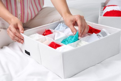 Photo of Woman putting underwear into organizer on bed, closeup