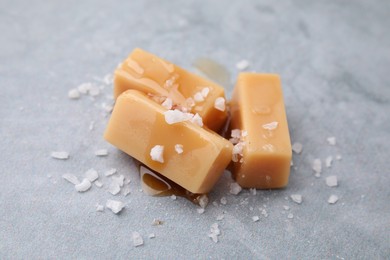 Yummy caramel candies and sea salt on grey table, closeup