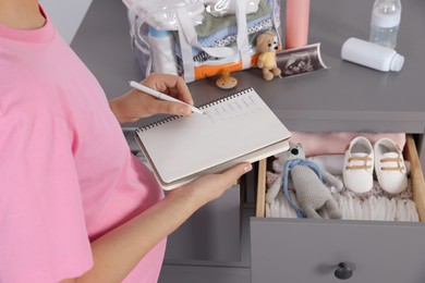 Photo of Pregnant woman preparing list of necessary items to bring into maternity hospital at home, closeup