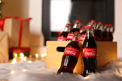 MYKOLAIV, UKRAINE - JANUARY 18, 2021: Wooden 
 crate with Coca-Cola bottles on floor in room