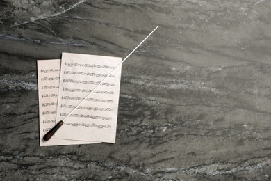 Conductor's baton and sheet music on grey table, flat lay. Space for text
