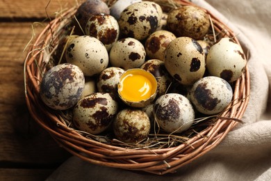 Photo of Wicker bowl with quail eggs and straw on table, closeup