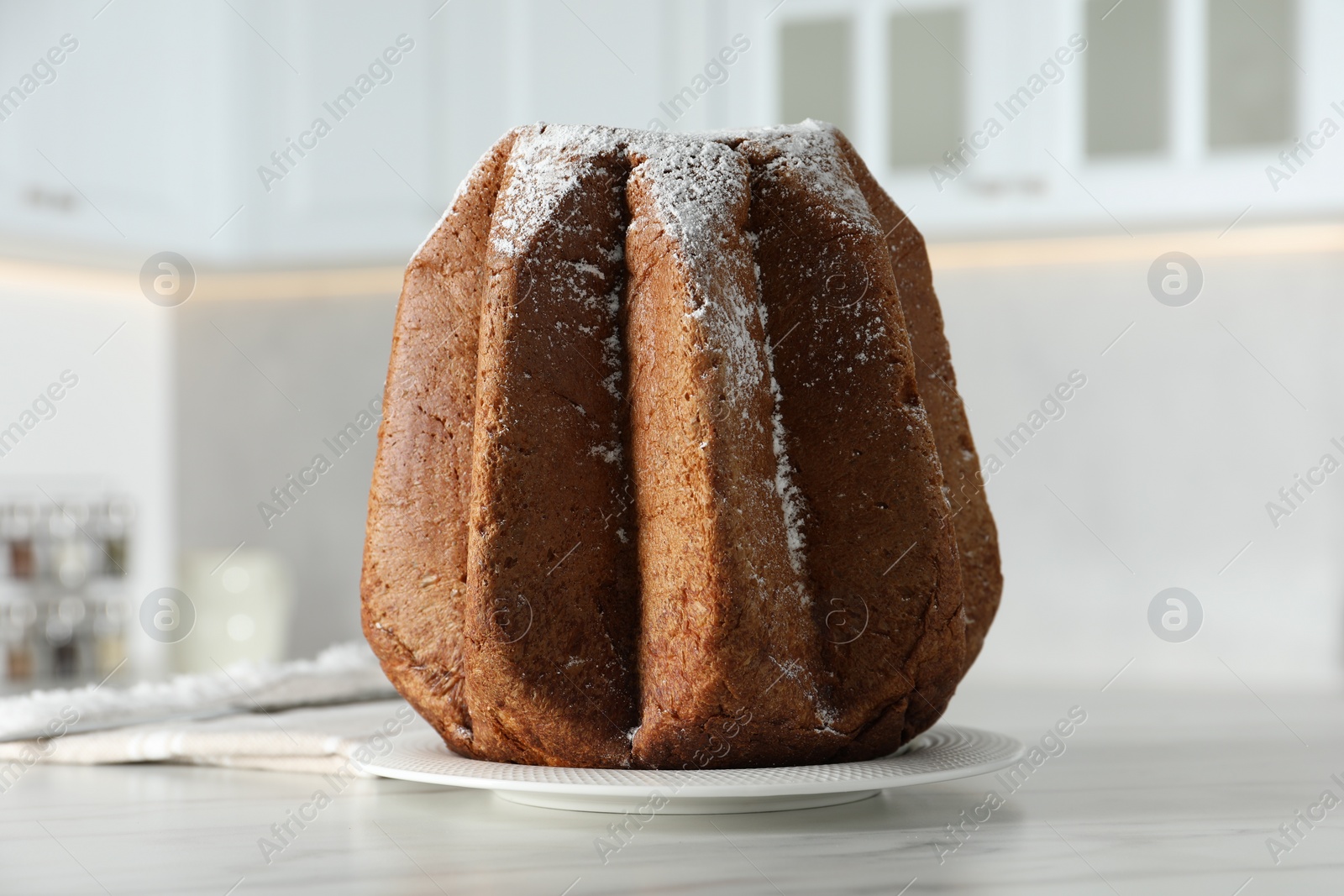 Photo of Delicious Pandoro cake decorated with powdered sugar on white table in kitchen, closeup. Traditional Italian pastry