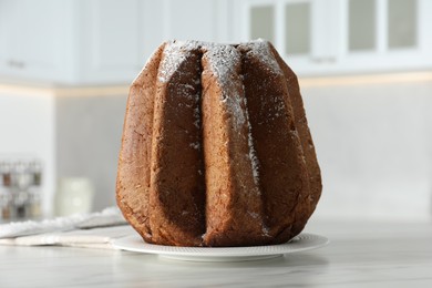 Delicious Pandoro cake decorated with powdered sugar on white table in kitchen, closeup. Traditional Italian pastry