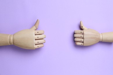 Wooden mannequin hands on lilac background, flat lay