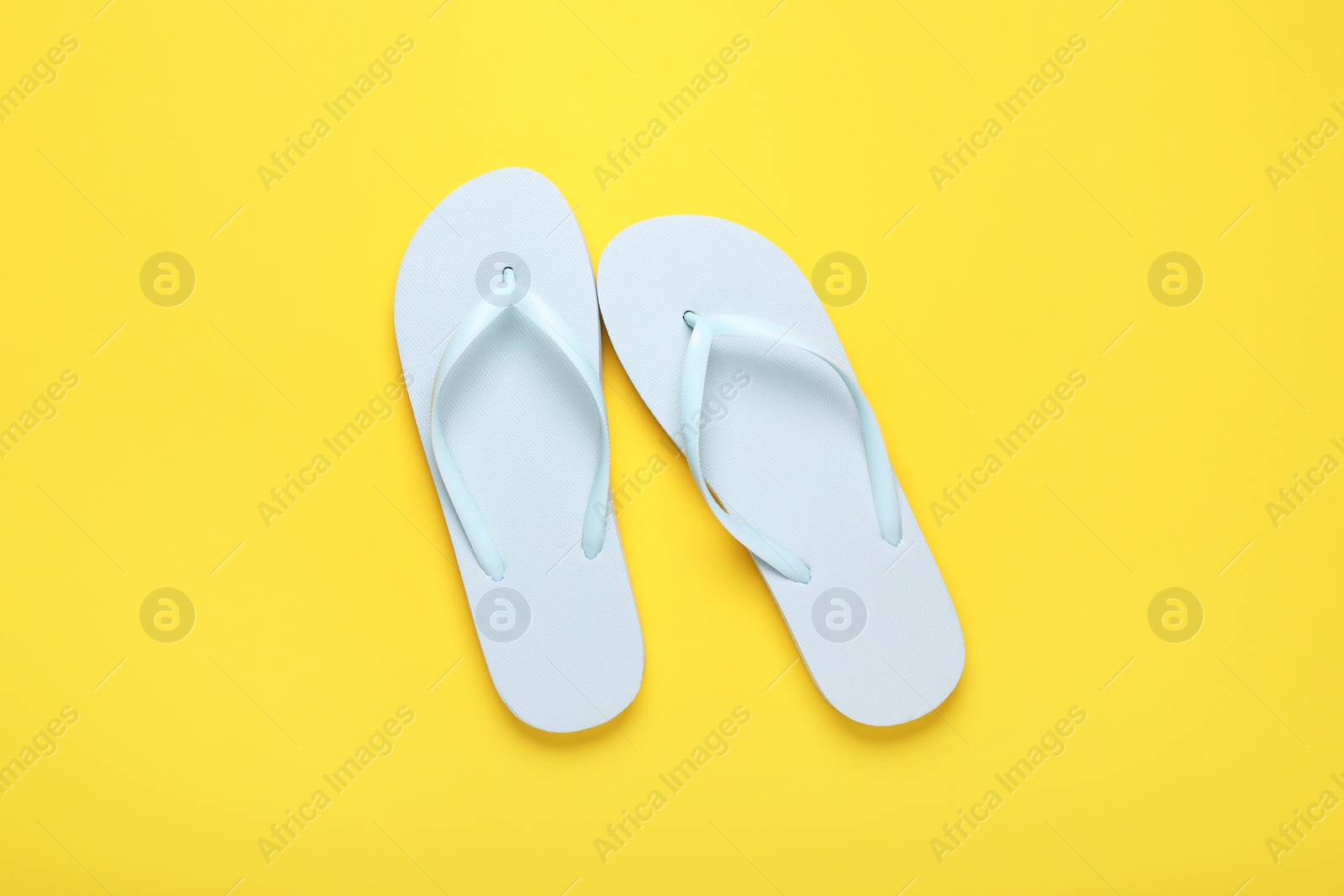 Photo of Stylish white flip flops on yellow background, top view