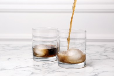 Photo of Pouring cocktail into glass with ice ball on white marble table