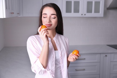 Happy young woman with fresh ripe tangerines in kitchen
