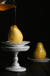 Pouring sweet syrup onto fresh ripe pear on table against dark background