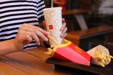 Photo of MYKOLAIV, UKRAINE - AUGUST 11, 2021: Woman with McDonald's French fries and drink at table in cafe, closeup