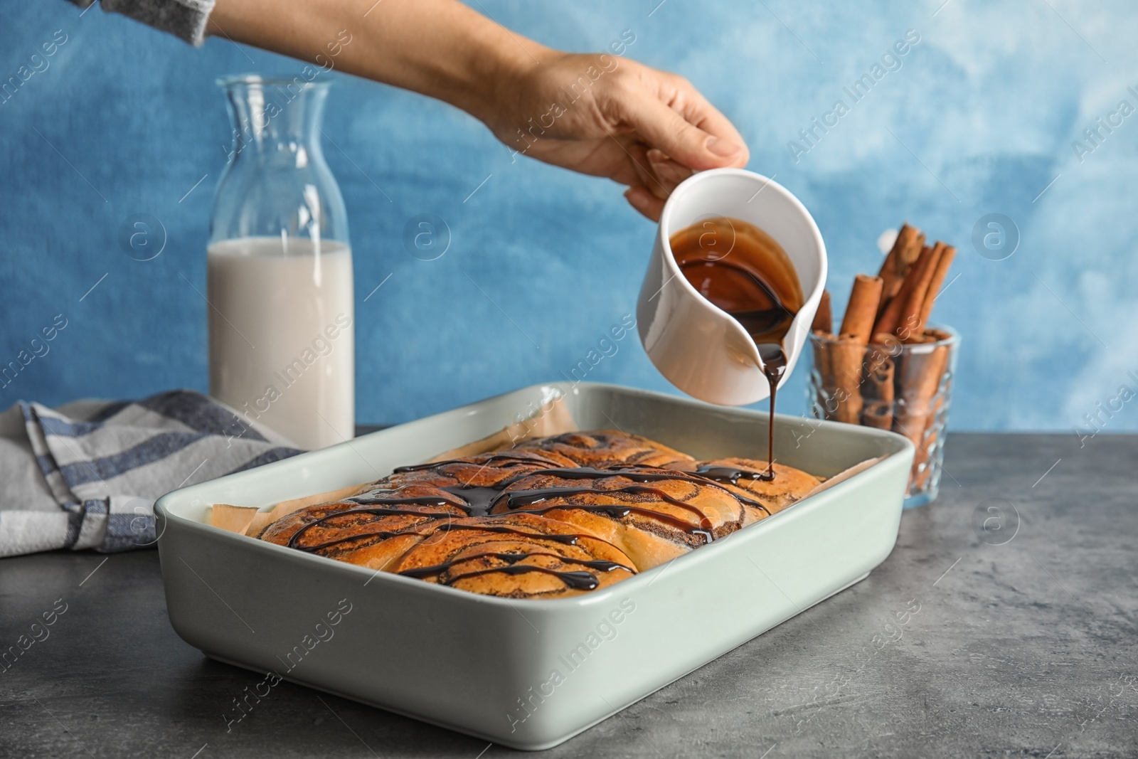 Photo of Woman pouring chocolate syrup onto freshly baked cinnamon rolls on table, closeup