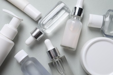 Many bottles of cosmetic serum on light grey background, flat lay