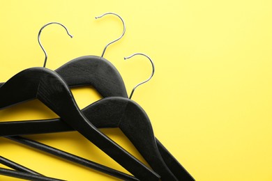 Black hangers on yellow background, top view. Space for text