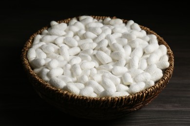 Photo of White silk cocoons in wicker bowl on wooden table