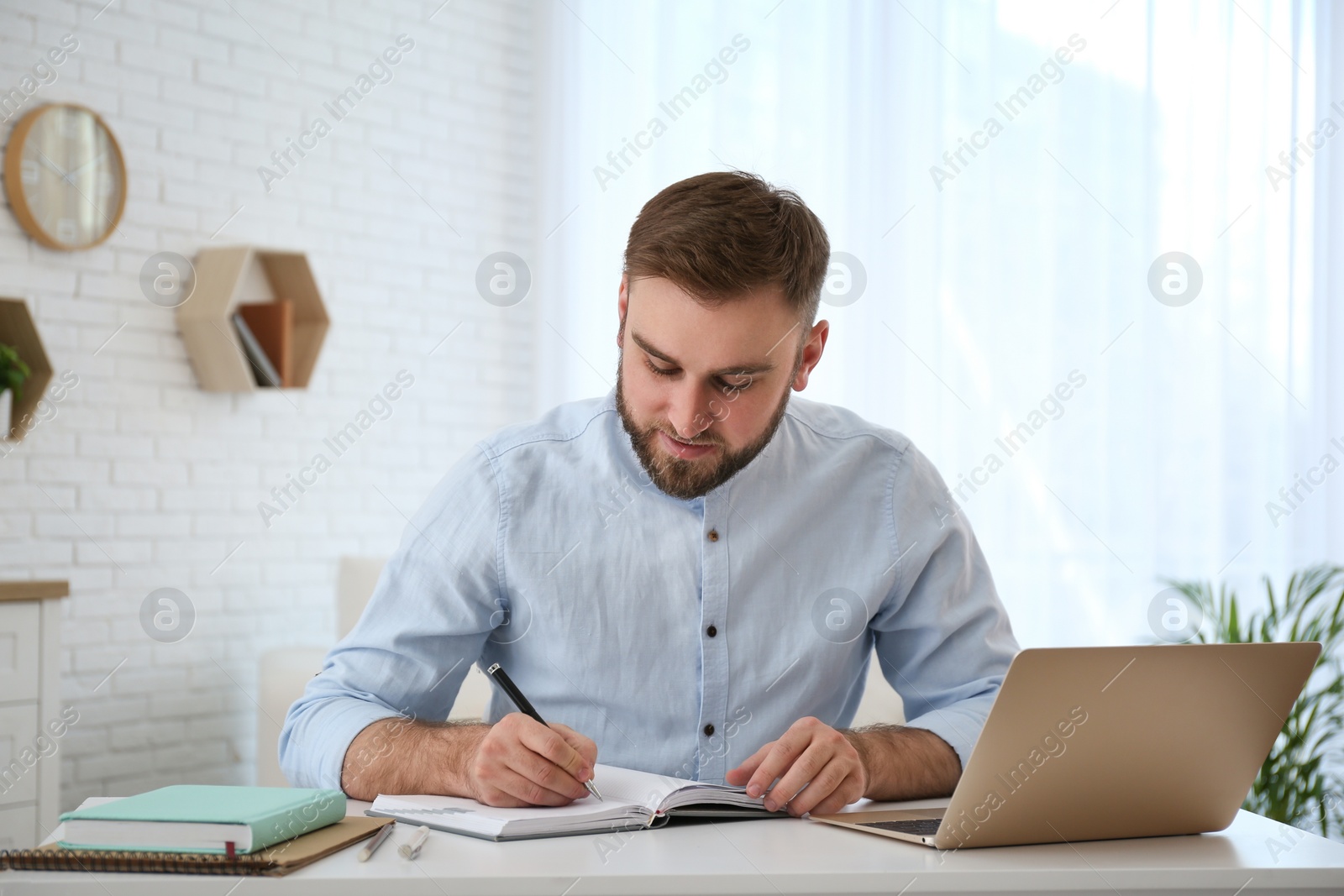 Photo of Young man taking notes during online webinar at table indoors