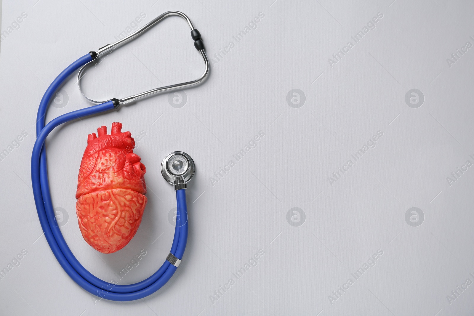 Photo of Stethoscope, heart model on grey background, flat lay with space for text. Cardiology concept