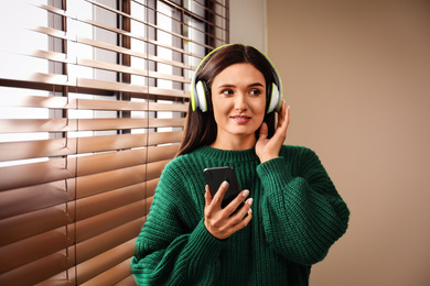 Young woman listening to audiobook near window indoors