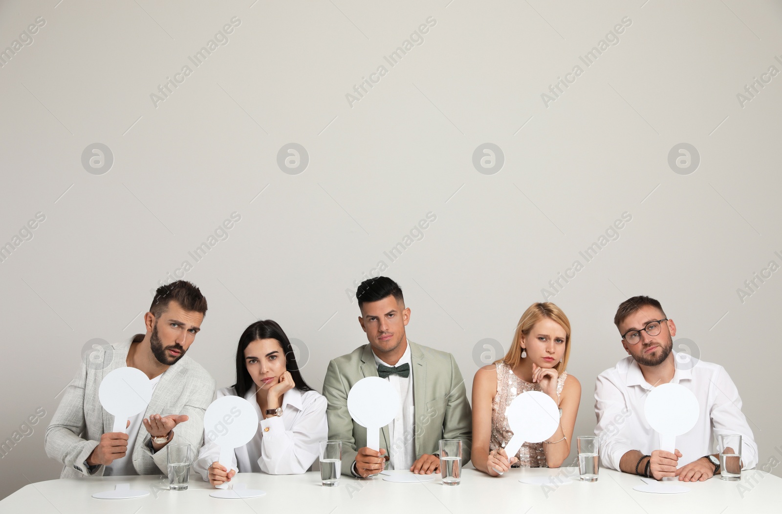 Photo of Panel of disappointed judges holding blank score signs at table on beige background. Space for text