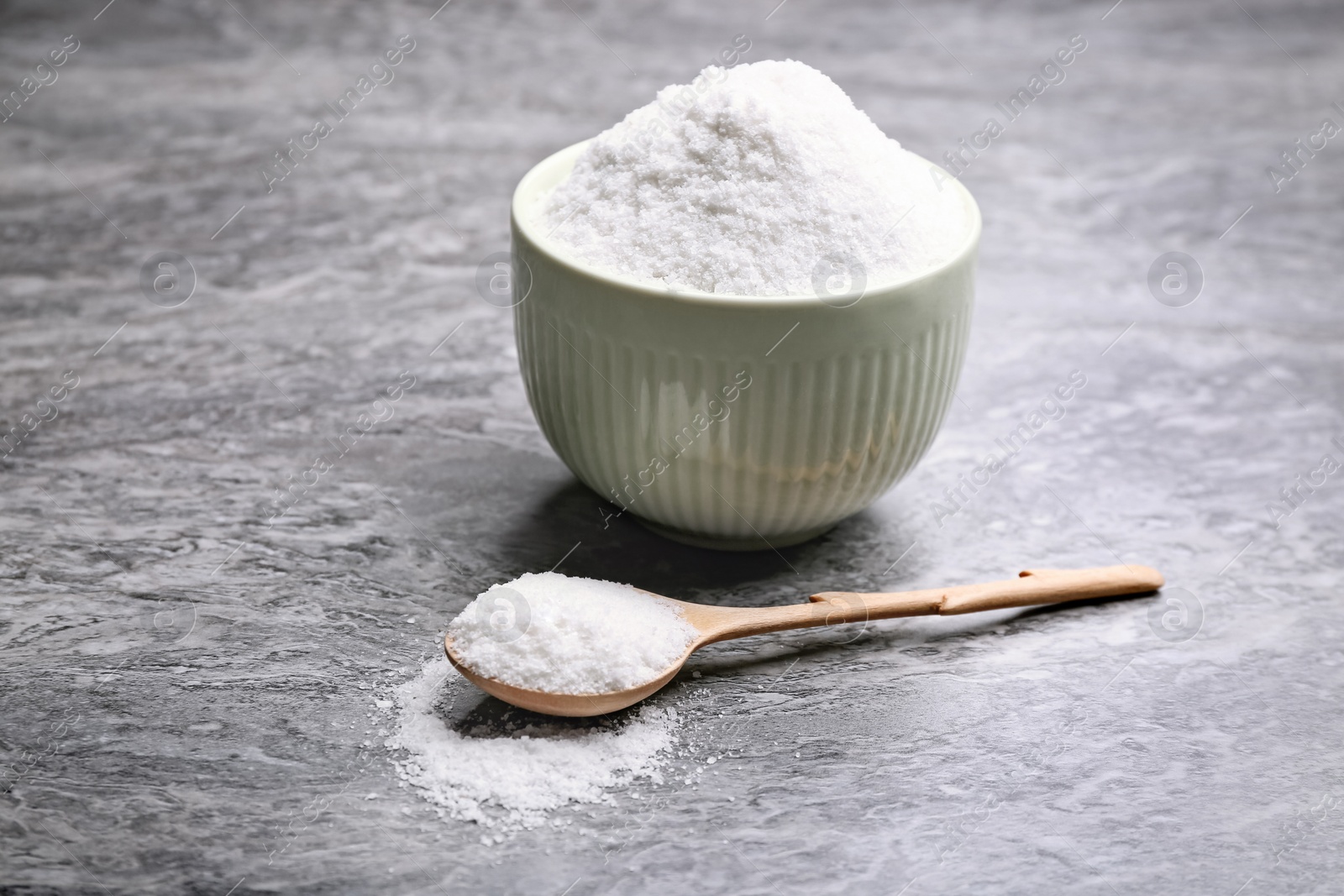 Photo of Bowl and spoon with salt on grey table, closeup