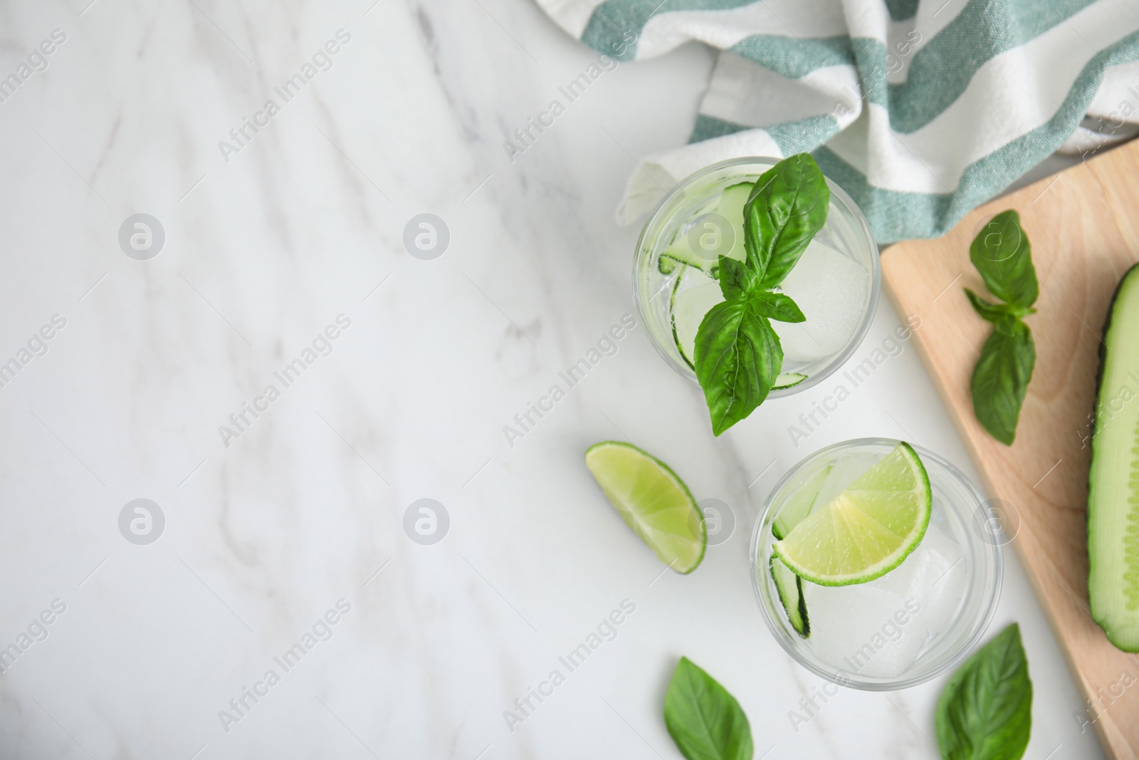 Photo of Tasty fresh cucumber water with sliced lime and basil on white marble table, flat lay. Space for text