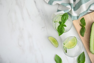 Tasty fresh cucumber water with sliced lime and basil on white marble table, flat lay. Space for text