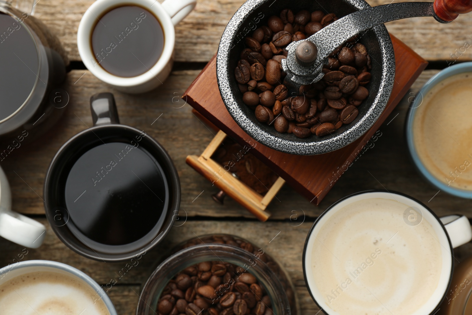 Photo of Different coffee drinks in cups, beans and manual grinder on wooden table, flat lay