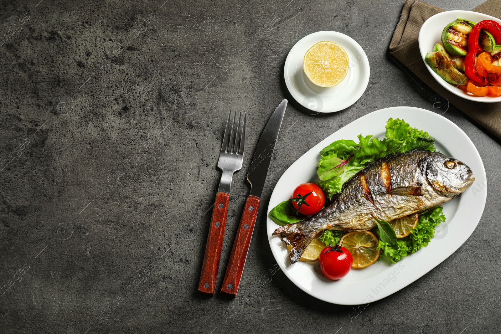 Photo of Delicious roasted fish with lemon and vegetables on dark grey table, flat lay. Space for text