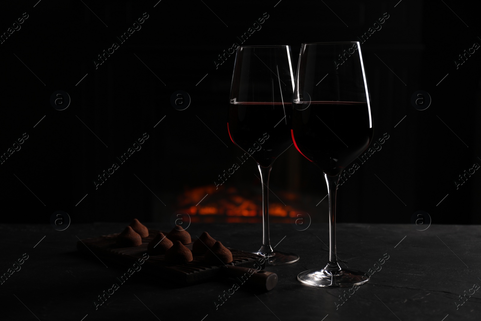 Photo of Glasses of red wine and chocolate truffles on black table in darkness, space for text