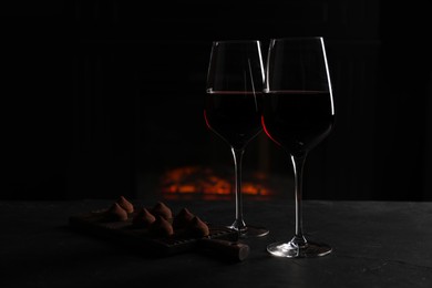 Glasses of red wine and chocolate truffles on black table in darkness, space for text
