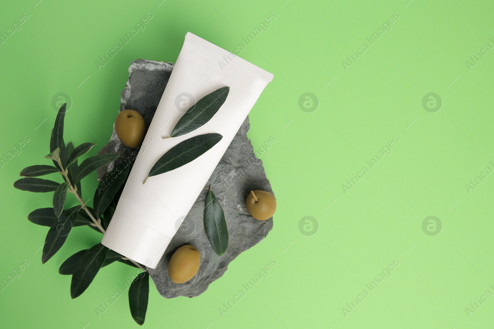 Photo of Tube of cream and olives on light green background, flat lay. Space for text