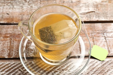 Photo of Tea bag in glass cup on wooden table, closeup