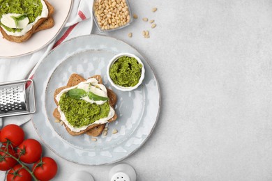 Tasty bruschettas with cream cheese, pesto sauce and fresh basil on light gray table, flat lay. Space for text