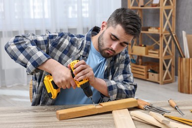 Photo of Young handyman working with electric drill at table in workshop