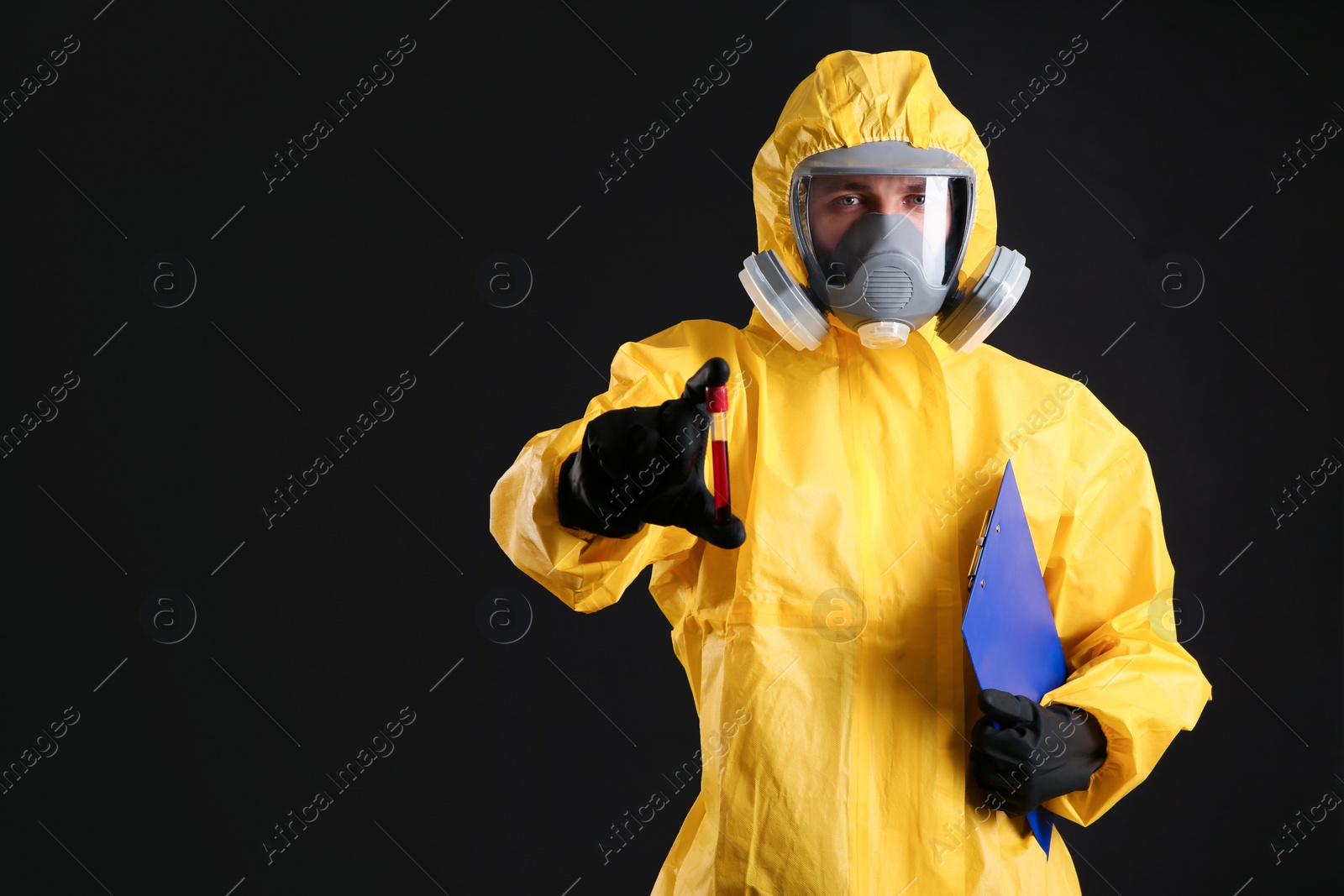 Photo of Man in chemical protective suit holding test tube of blood sample on black background, space for text. Virus research