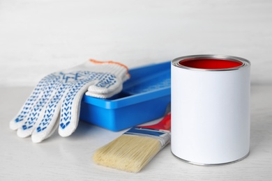 Photo of Can of paint with brush, tray and gloves on white wooden table. Space for text