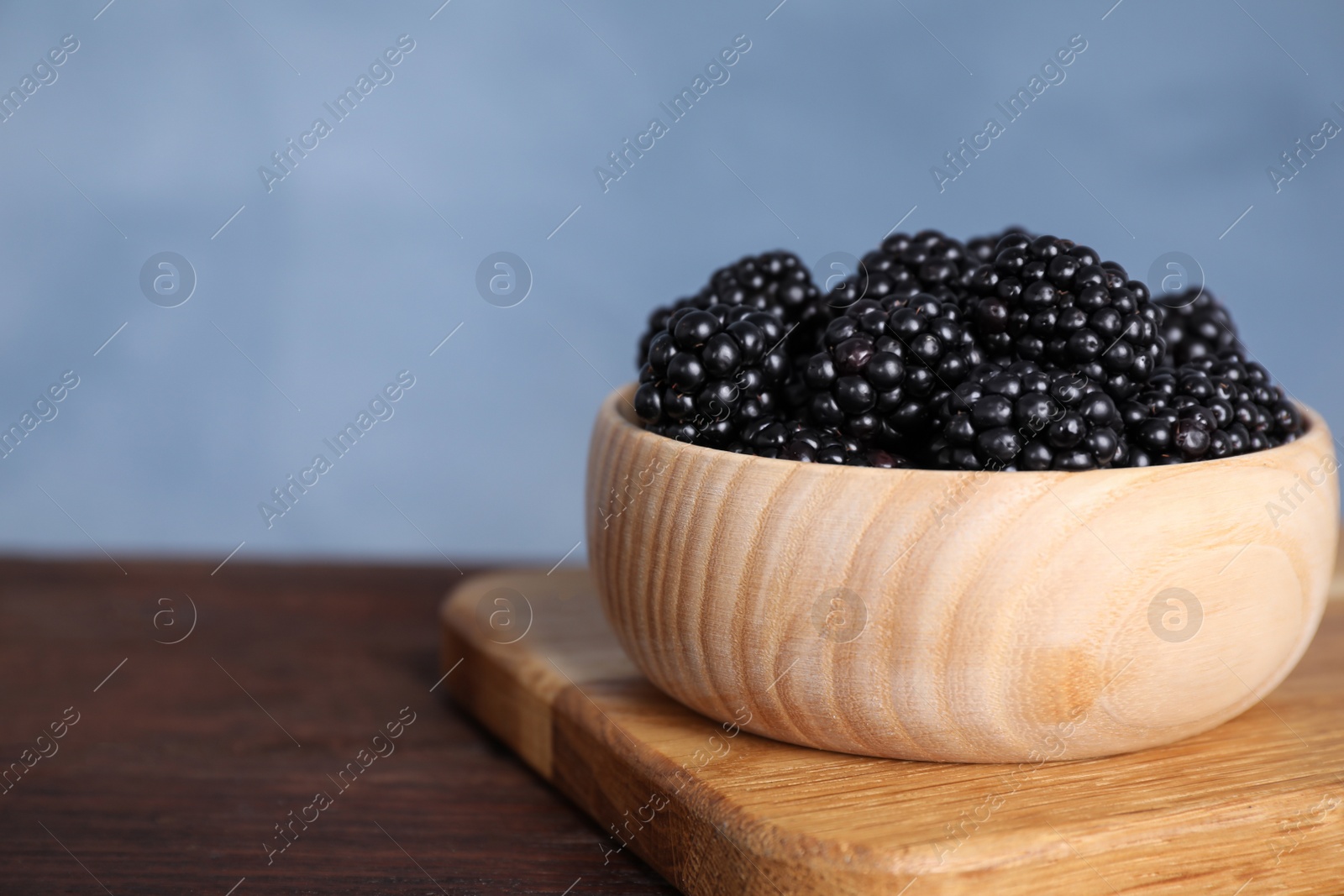 Photo of Fresh ripe blackberries in bowl on wooden table, closeup. Space for text