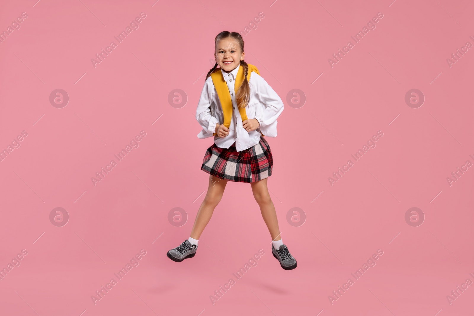 Photo of Happy schoolgirl with backpack jumping on pink background