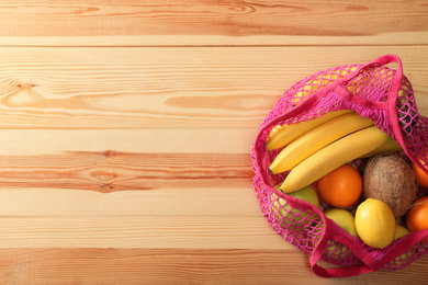 Photo of Net bag with fruits on wooden table, top view. Space for text