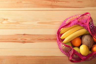 Net bag with fruits on wooden table, top view. Space for text