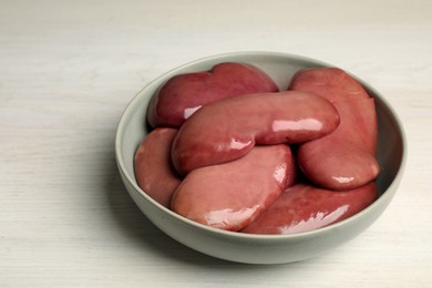 Photo of Bowl with fresh raw pork kidneys on white wooden table, closeup