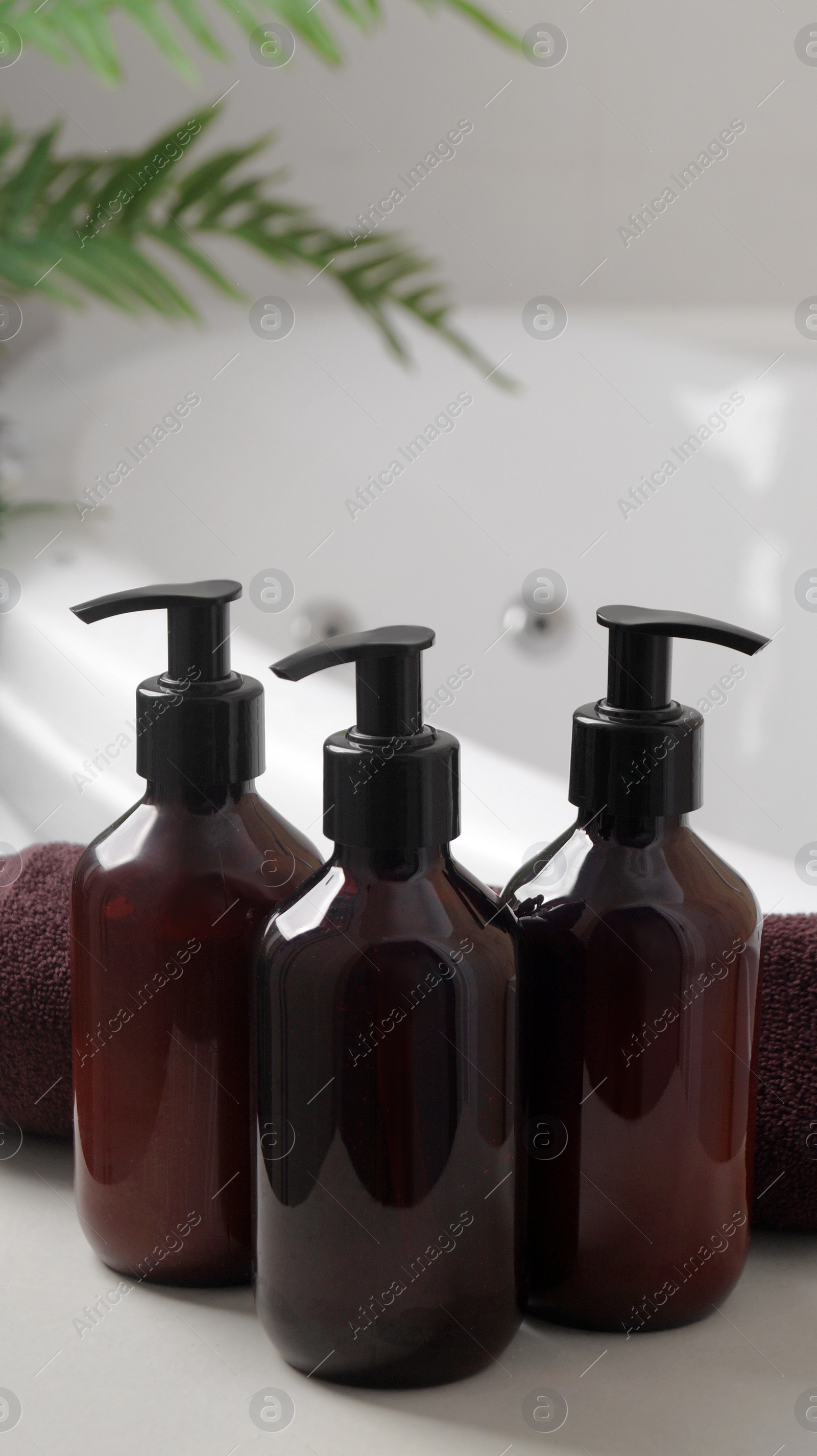 Photo of Bath foam and other personal hygiene products in bottles and rolled towel on small table in bathroom