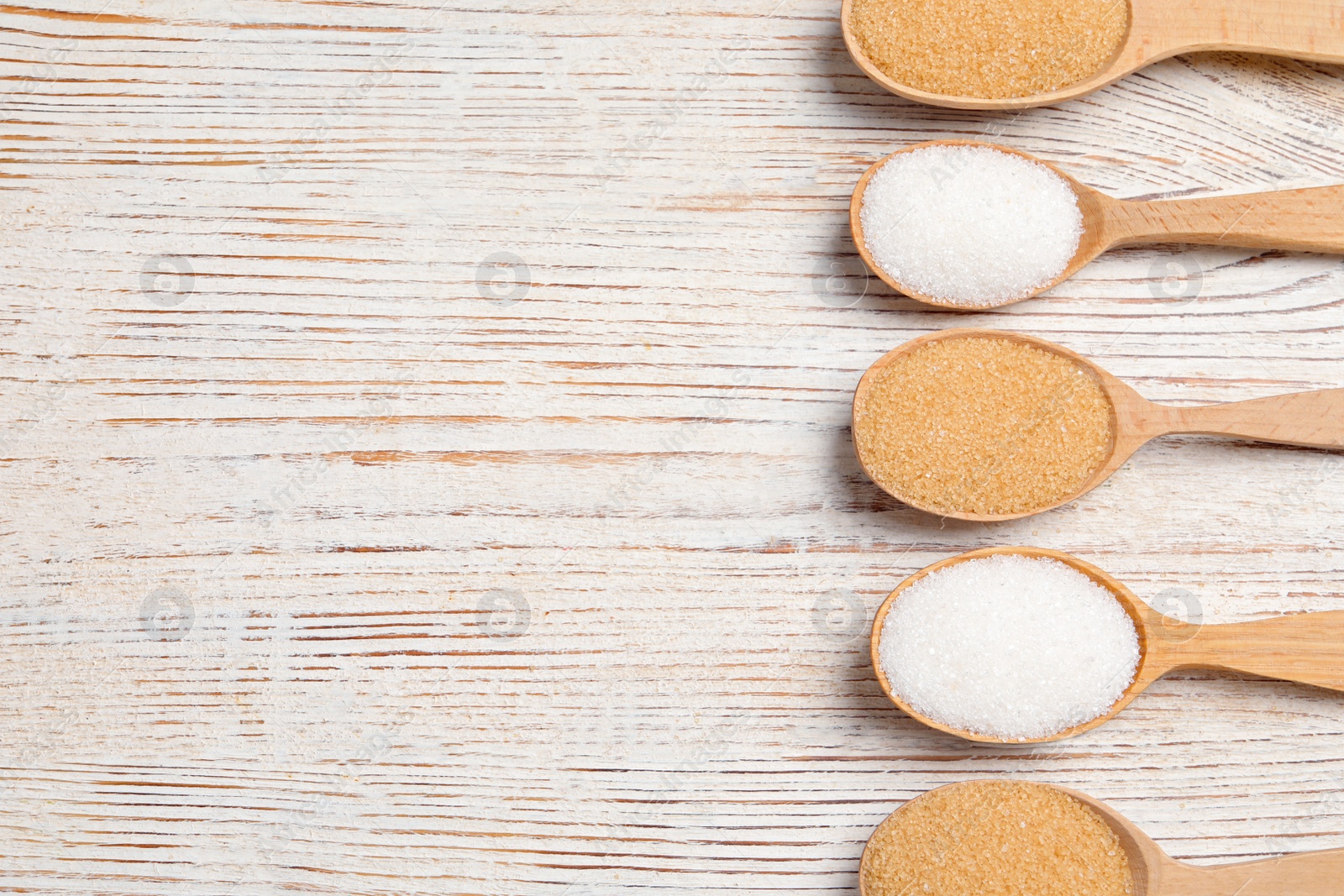 Photo of Spoons with white and brown granulated sugar on light wooden table, flat lay. Space for text