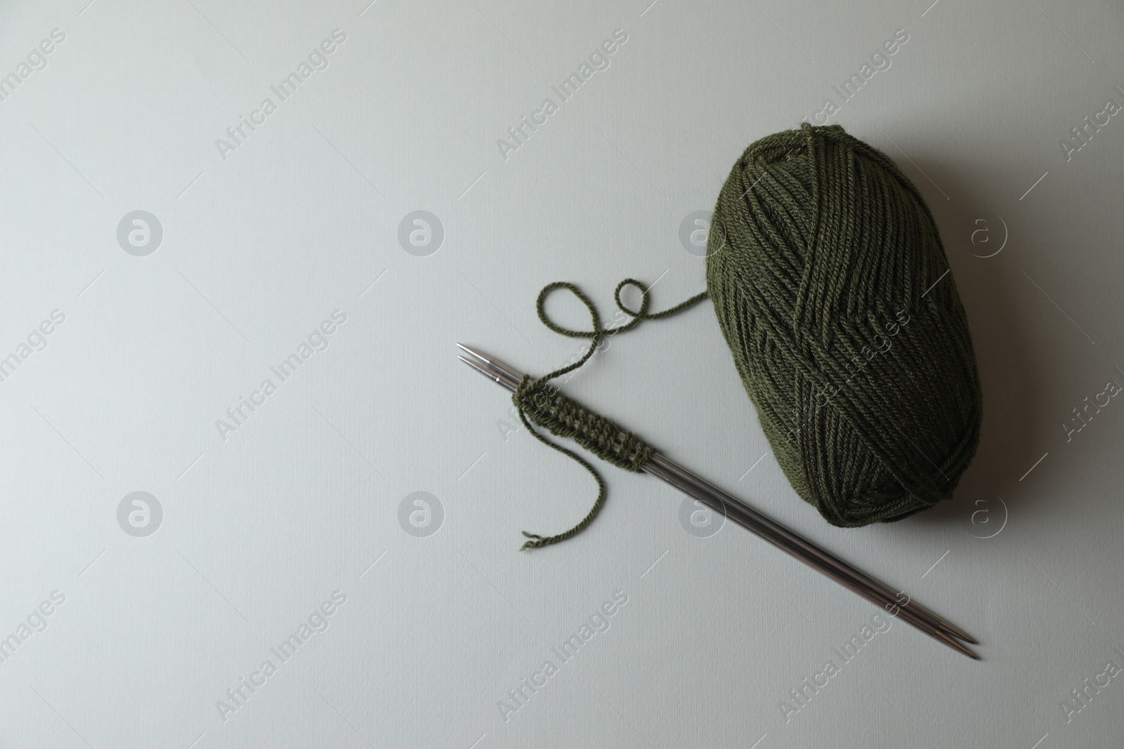 Photo of Soft green yarn, knitting and metal needles on light background, top view. Space for text