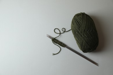 Soft green yarn, knitting and metal needles on light background, top view. Space for text