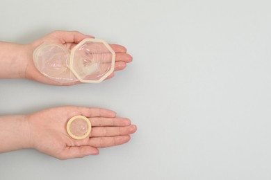 Photo of Woman with unrolled female and male condoms on light background, top view. Space for text
