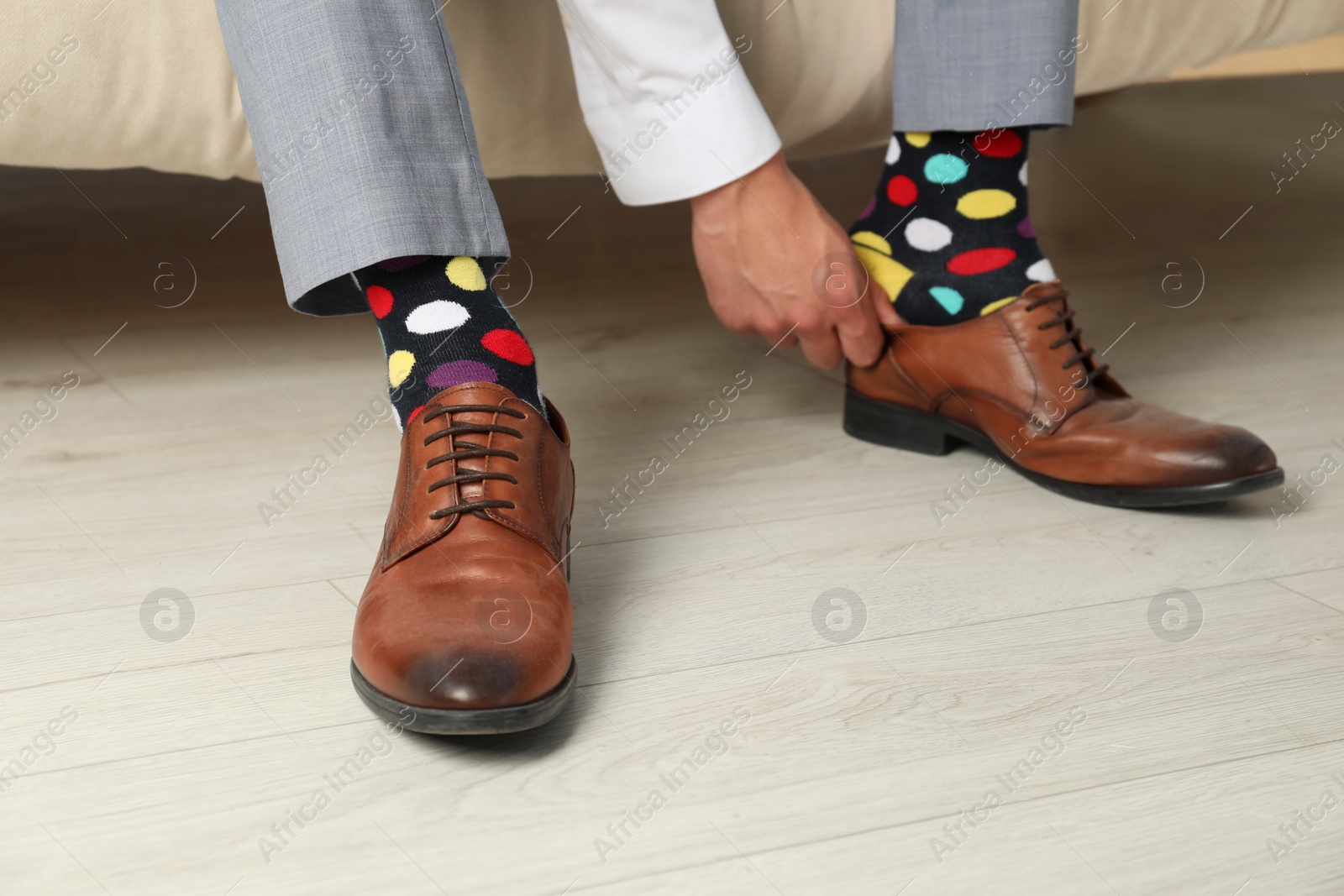 Photo of Man with colorful socks putting on stylish shoes indoors, closeup